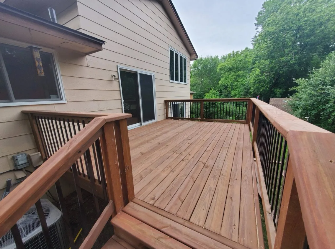 A large wooden deck with stairs leading up to it is in front of a house.