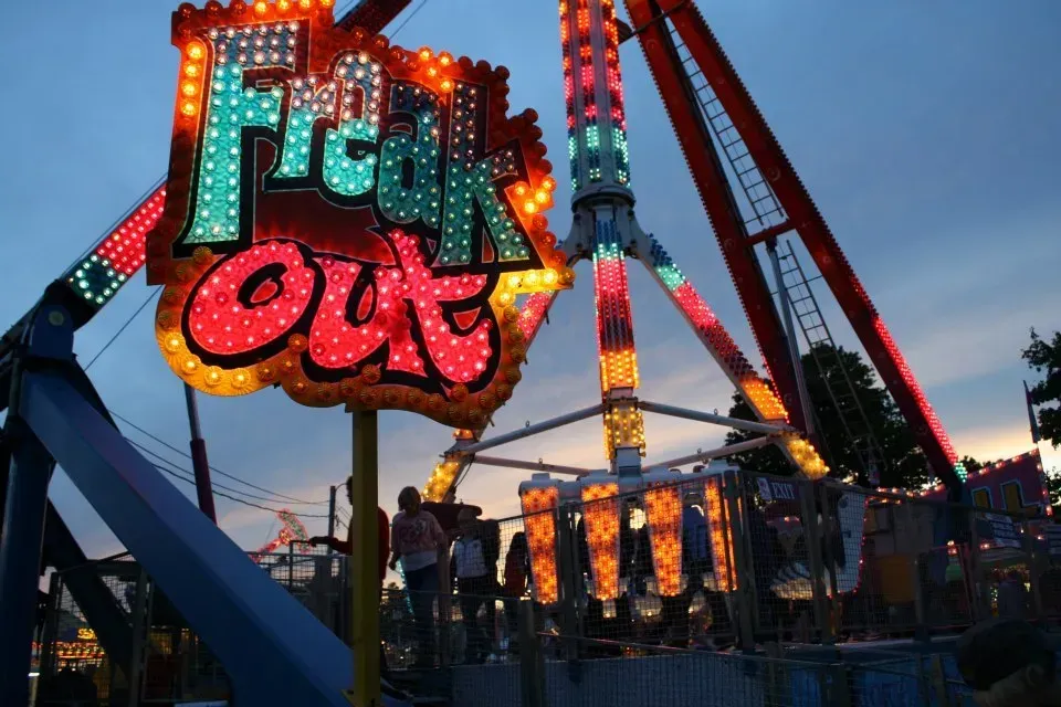 'Freak Out' amusement park ride with colorful lights at dusk. People are visible nearby.
