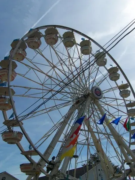 Ferris wheel against a partly cloudy blue sky, with flags and power lines visible.