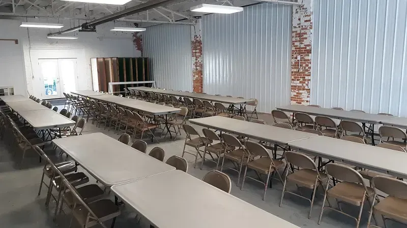 Long tables with chairs in a large, open room with metal and brick walls.