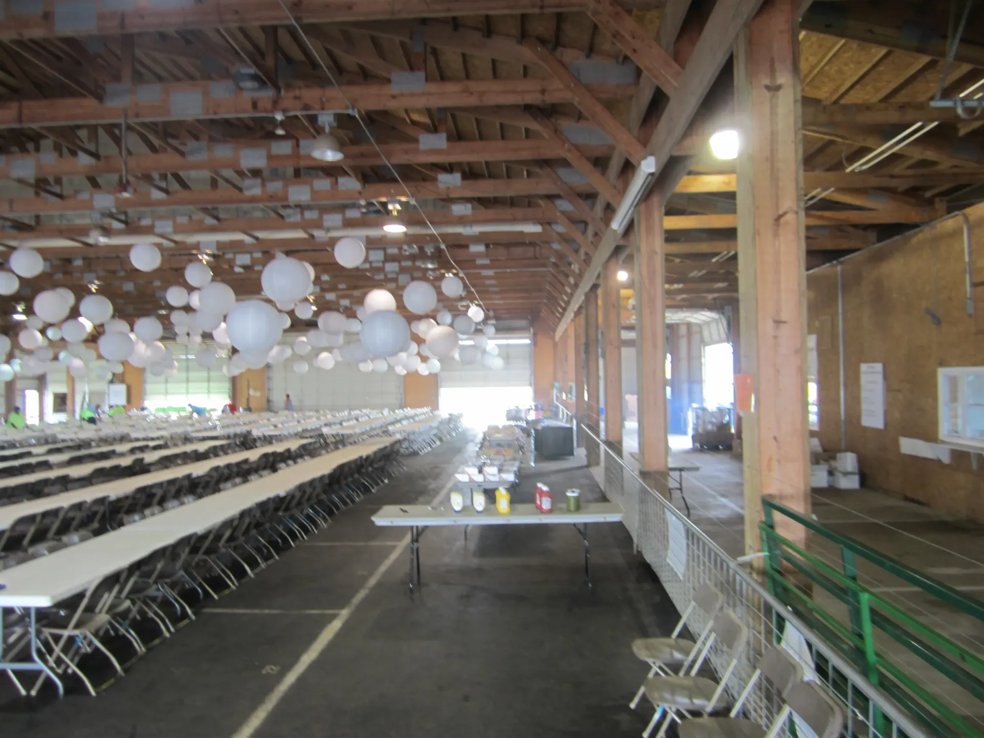 Long tables and chairs set up in a large hall, white paper lanterns hanging from the ceiling.