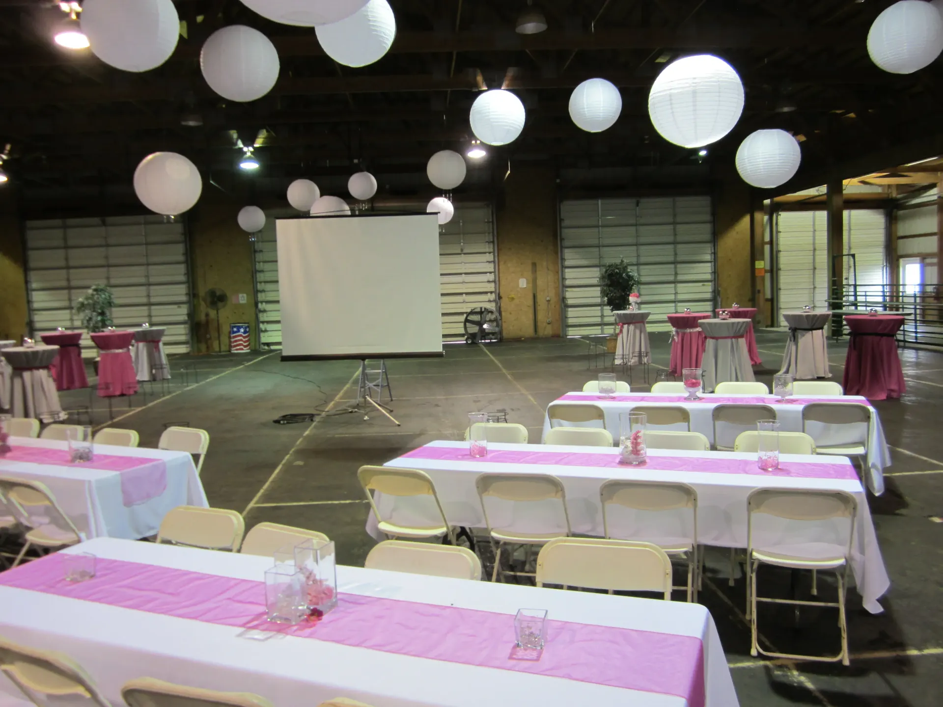 Event space with white paper lanterns, tables with pink runners, and folding chairs.