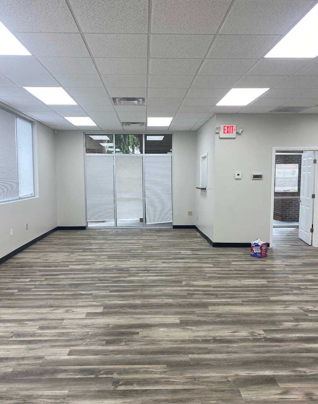 An empty room with a wooden floor and a red exit sign.