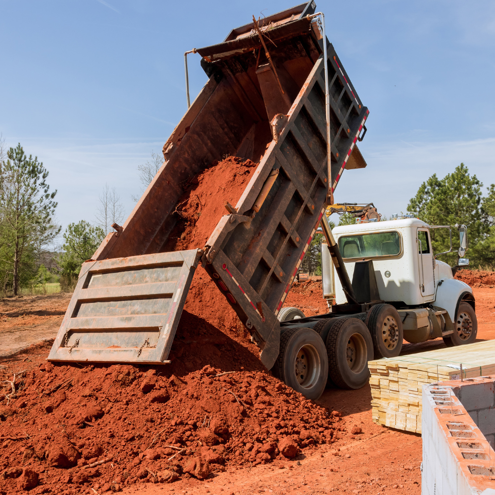 A dump truck is dumping dirt into a pile of bricks