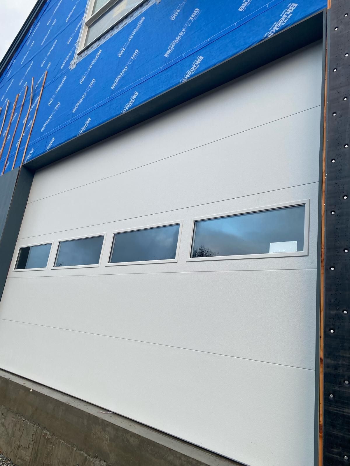 A low-angle view of a modern building facade featuring wood siding and grey panels with large, dark-framed glass windows.