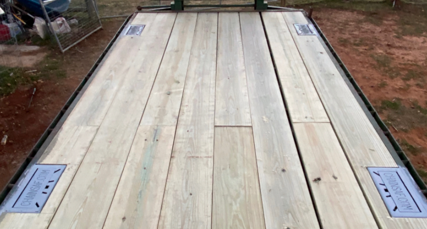 A flatbed trailer with new wooden deck boards and four metal tie-down anchor points installed on the edges.