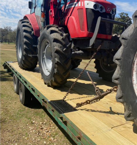 A red tractor secured with chains on a flatbed trailer outdoors on a sunny day.