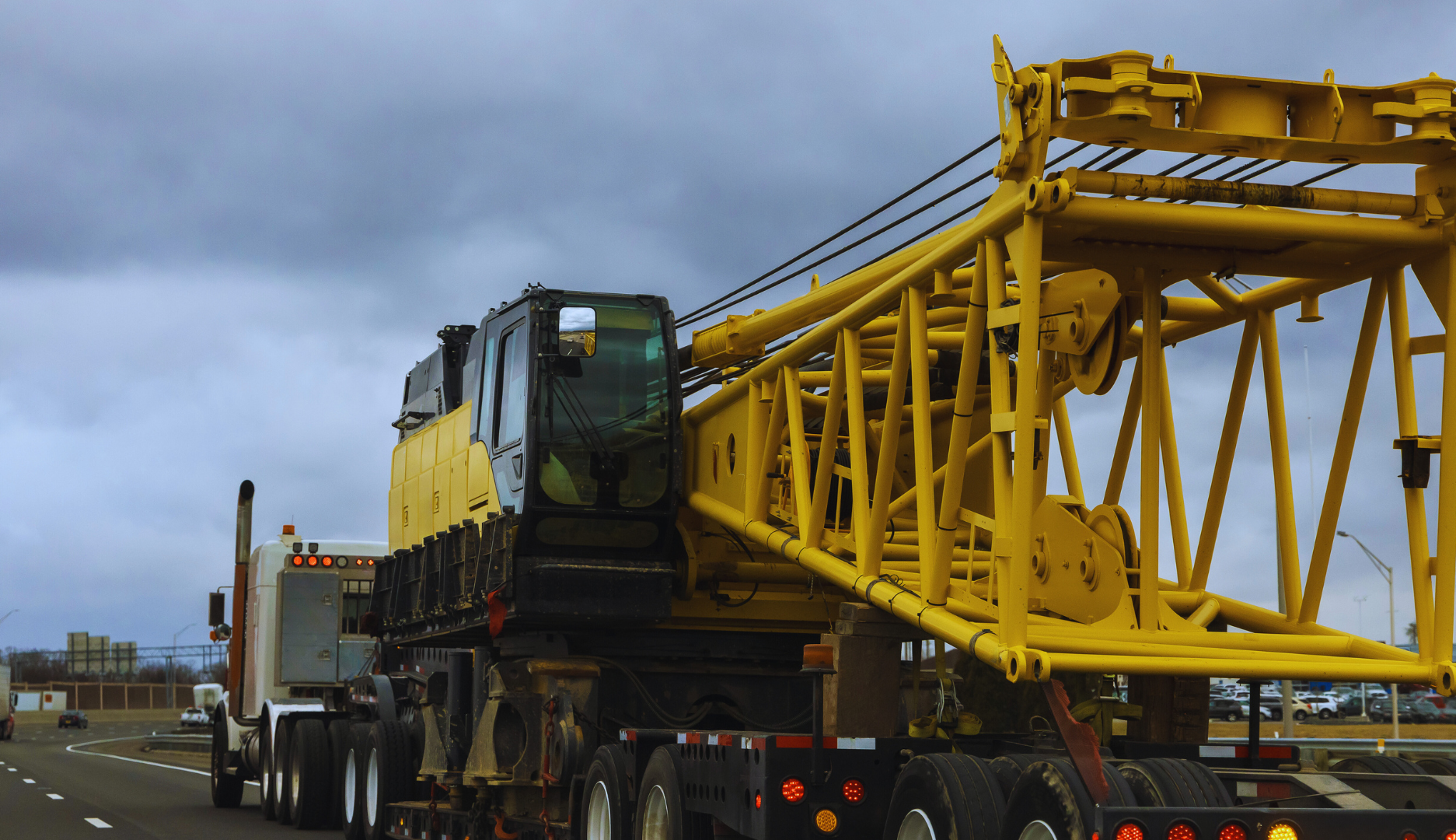 A large yellow crane upper assembly being transported on a flatbed trailer pulled by a semi-truck on a highway.