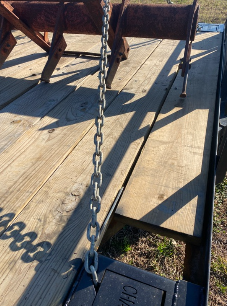 Close-up of a chain and trailer bed with sunlight and shadows. Parts of an implement are visible.