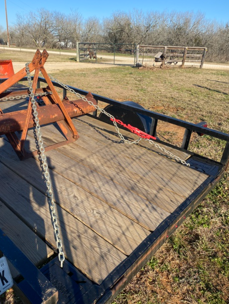 Trailer with rusty farm implement secured by chains on a grassy field.