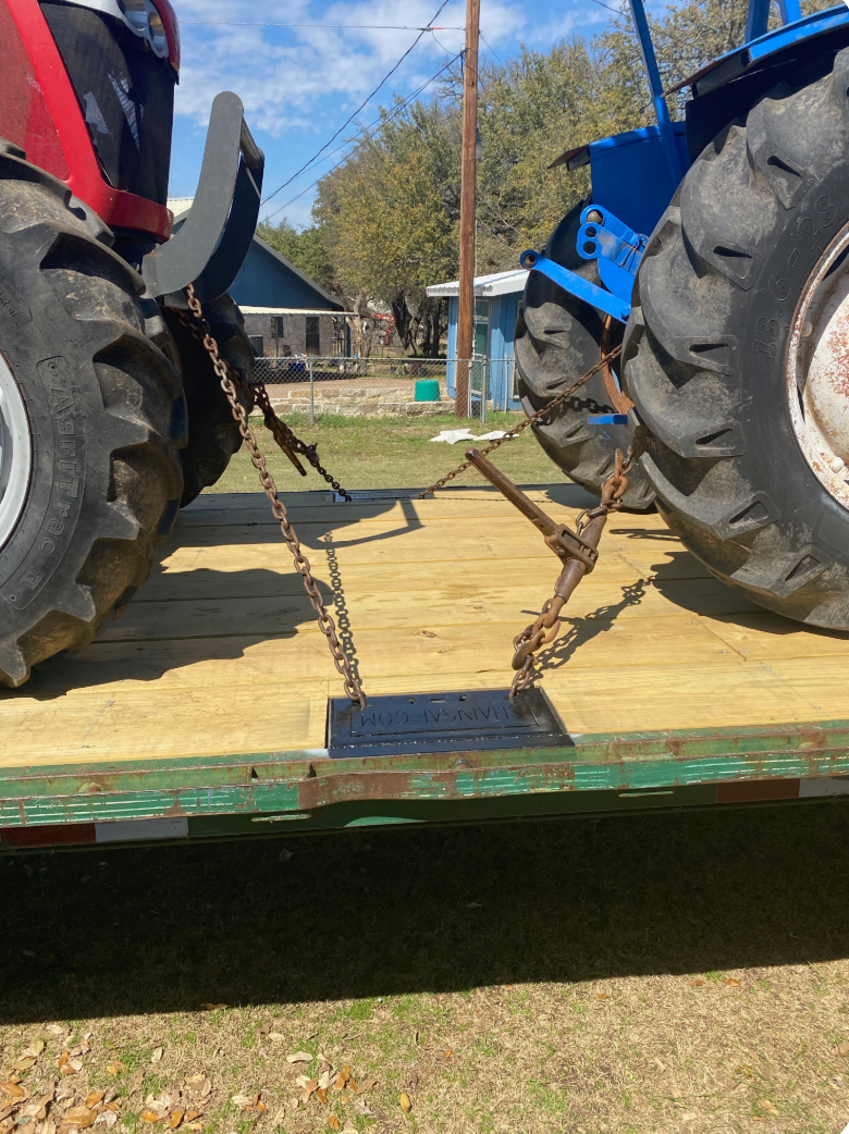 Two tractors chained to a trailer bed, likely for transport.