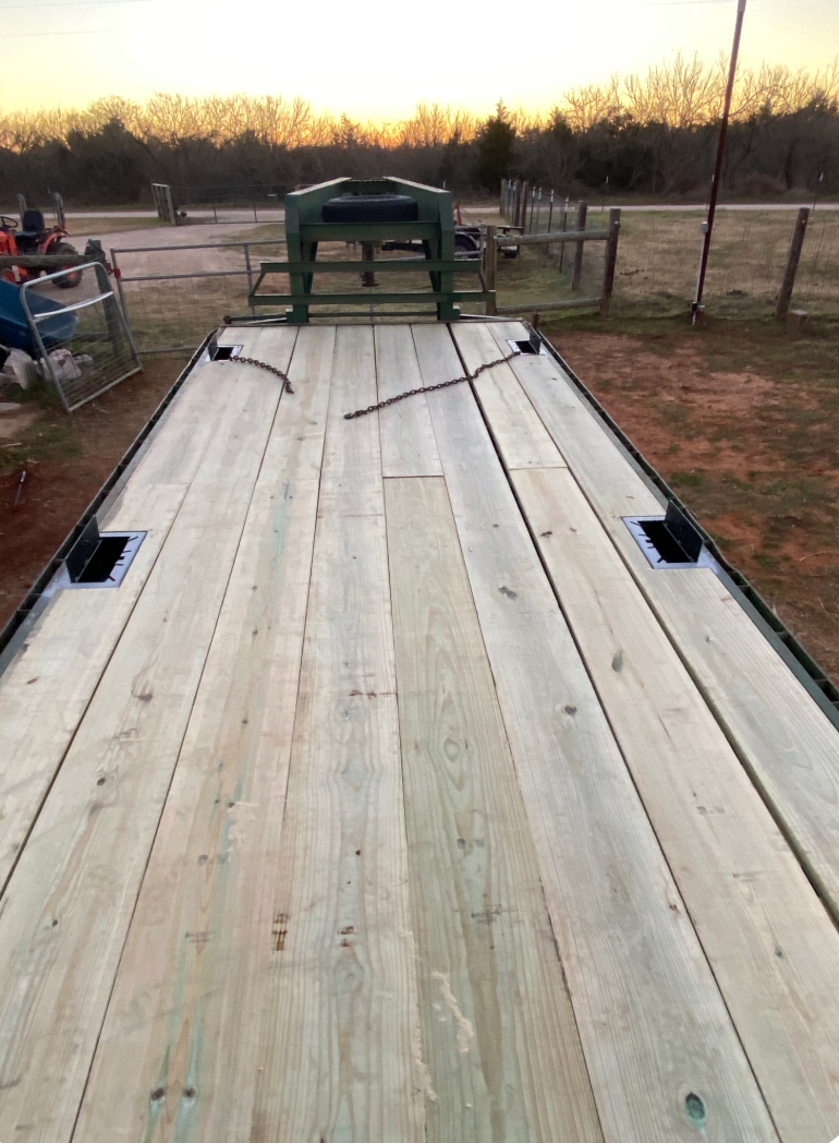 Flatbed trailer with wooden deck, viewed from front. The setting is outdoors.