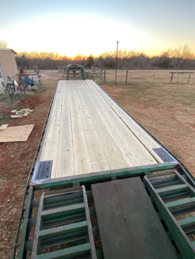 Green flatbed trailer with new wooden planks in a field.