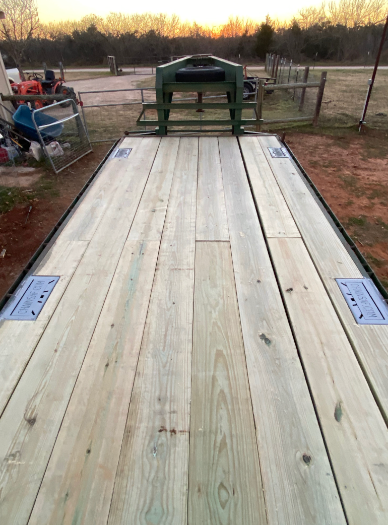 Wooden flatbed trailer, green metal neck, outdoors.