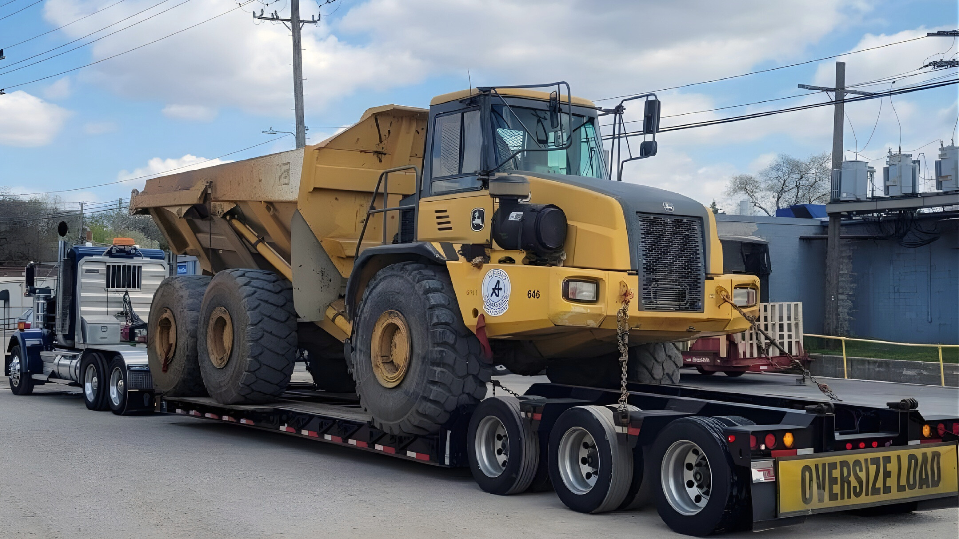 A large yellow dump truck loaded onto an oversized flatbed trailer attached to a semi-truck in an outdoor lot.