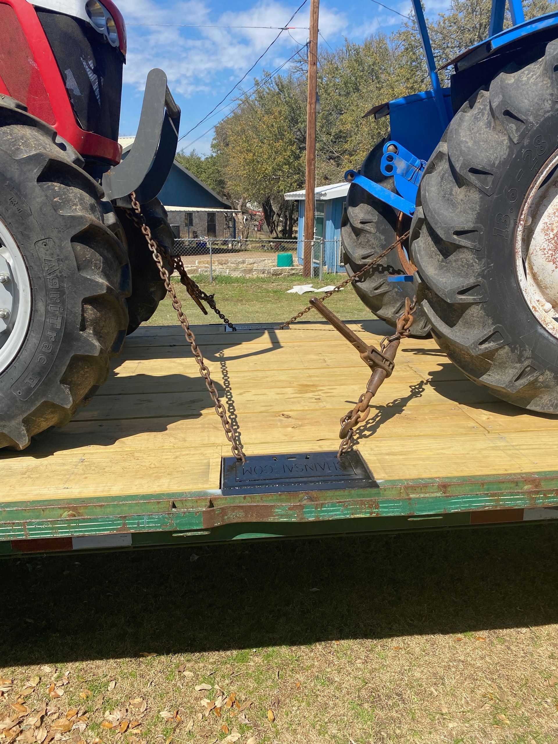 Two tractors secured on a trailer with chains, outdoors, sunny day.