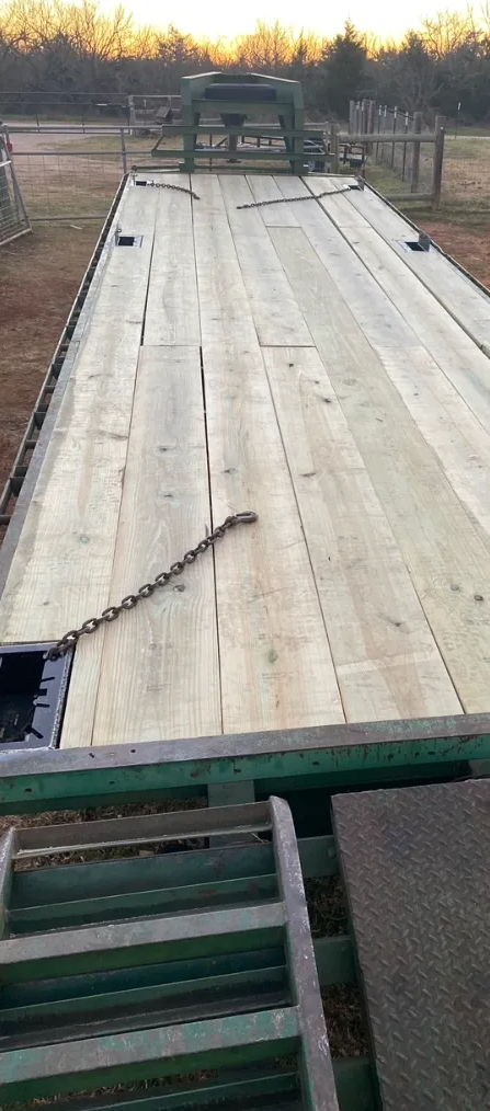 A red tractor secured with a red chain to the metal deck of a green trailer parked outdoors.