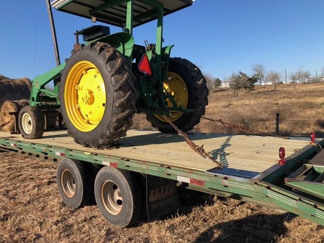 John Deere tractor secured with chains on a flatbed trailer, ready for transport.