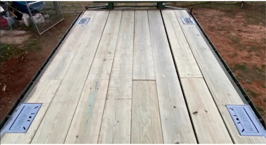 A flatbed trailer featuring new wooden decking with four warning labels applied to the boards.