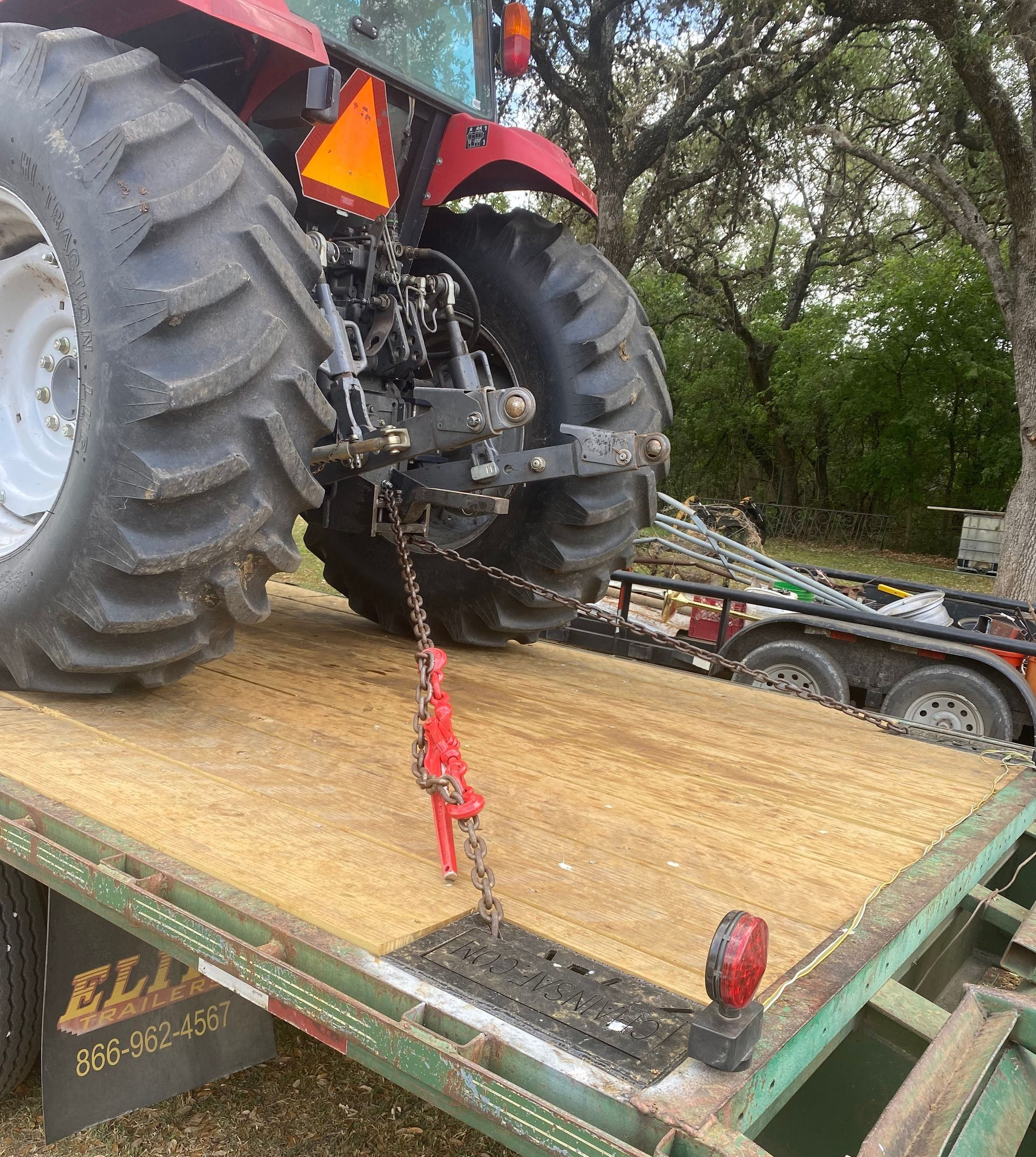 A red tractor secured with a red chain to the metal deck of a green trailer parked outdoors.