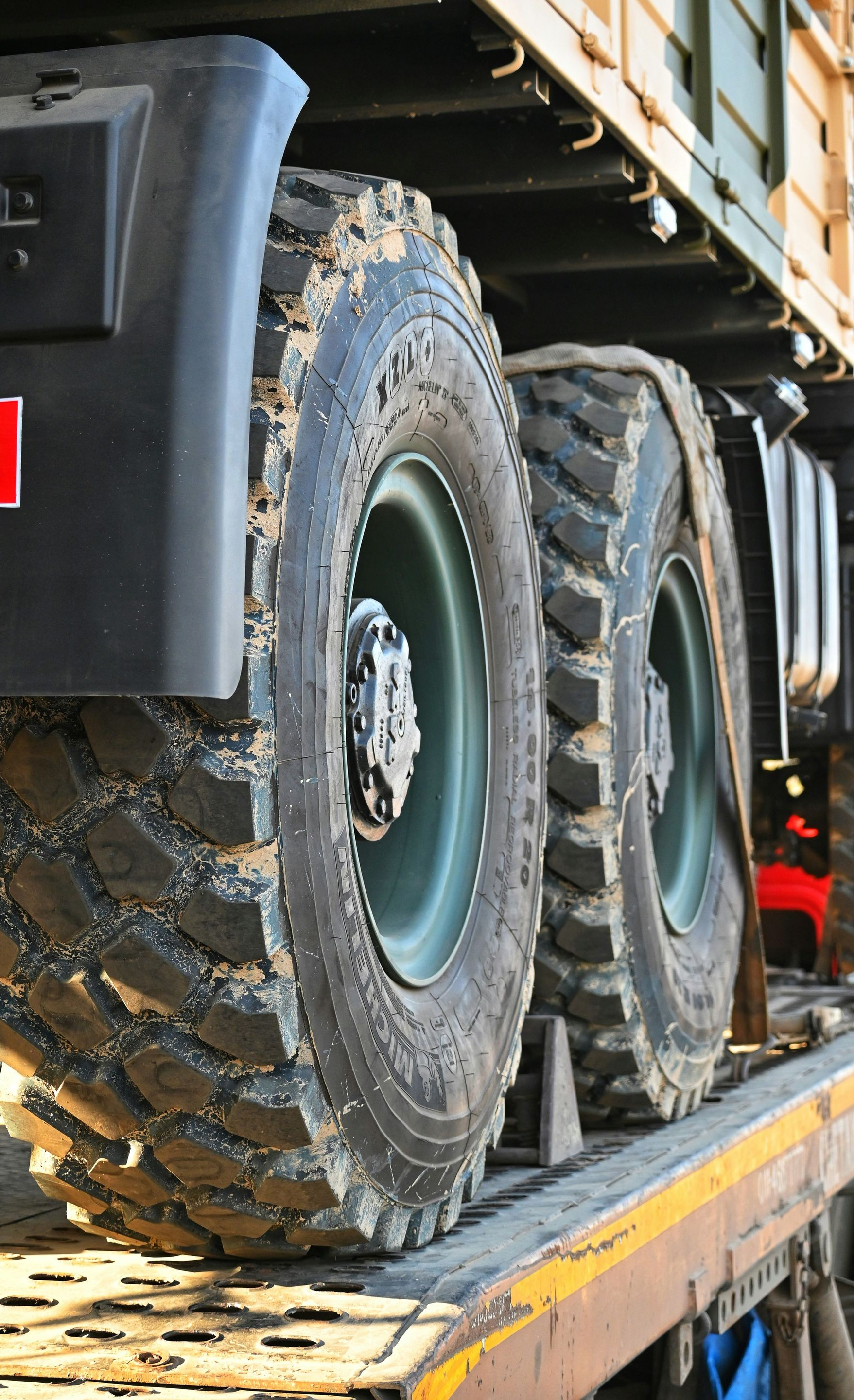 Close-up of two large, deep-tread military truck tires mounted on olive-drab rims, resting on a flatbed transport vehicle.