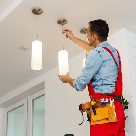 Kevin Walsh Master Electrician | A man in red overalls is fixing a light fixture