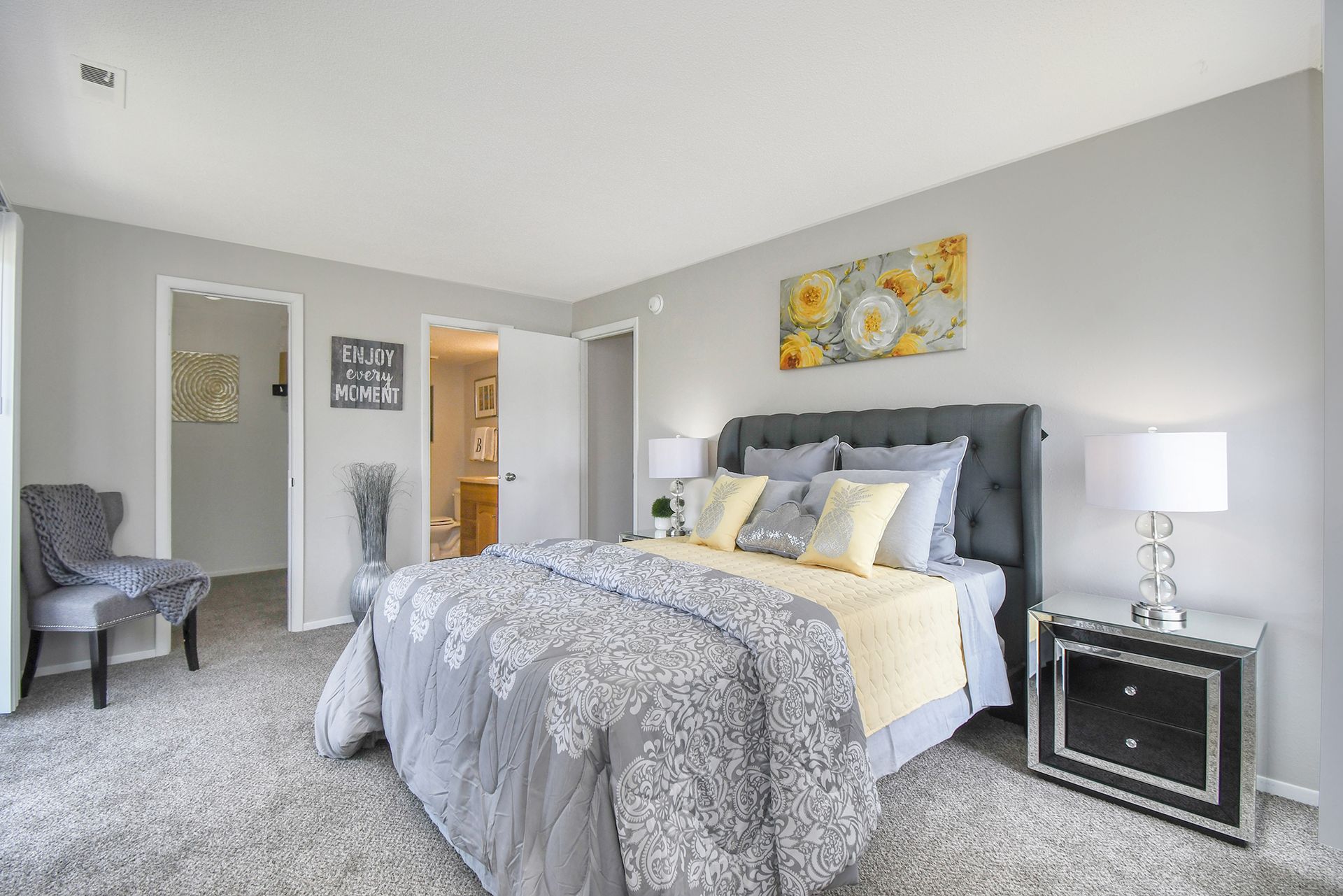Bedroom with gray walls, bed, nightstand, and chair. Yellow and gray bedding, floral art.