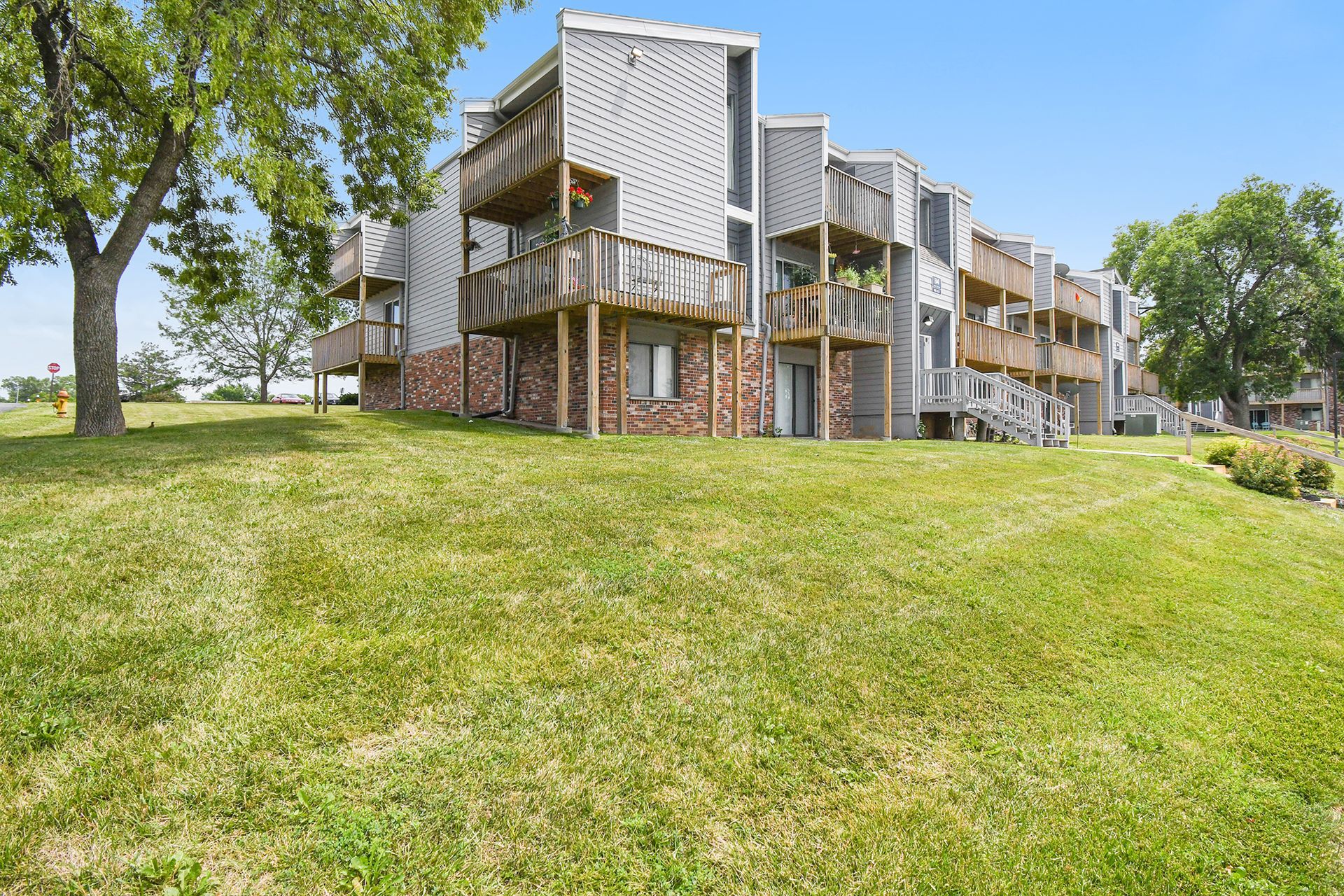 Apartment building with wooden balconies on a grassy hill under a blue sky.