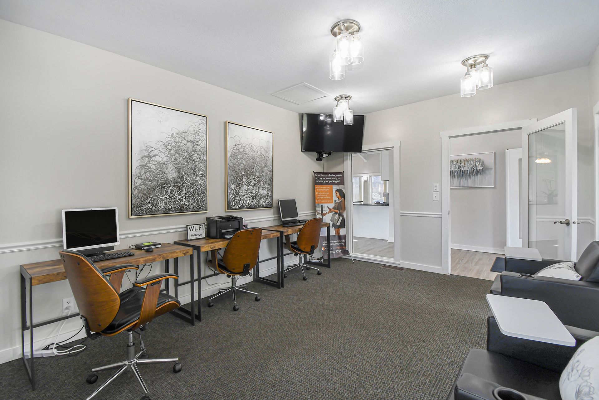 Computer room with desks, chairs, and artwork. A person is near an opening with a counter.