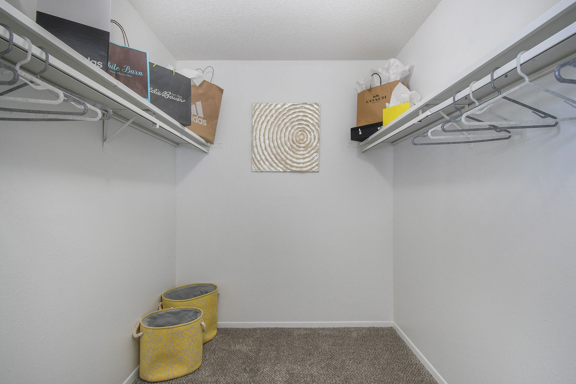 A walk-in closet with white walls, wire shelving, and shopping bags. Two yellow storage containers sit on the floor.