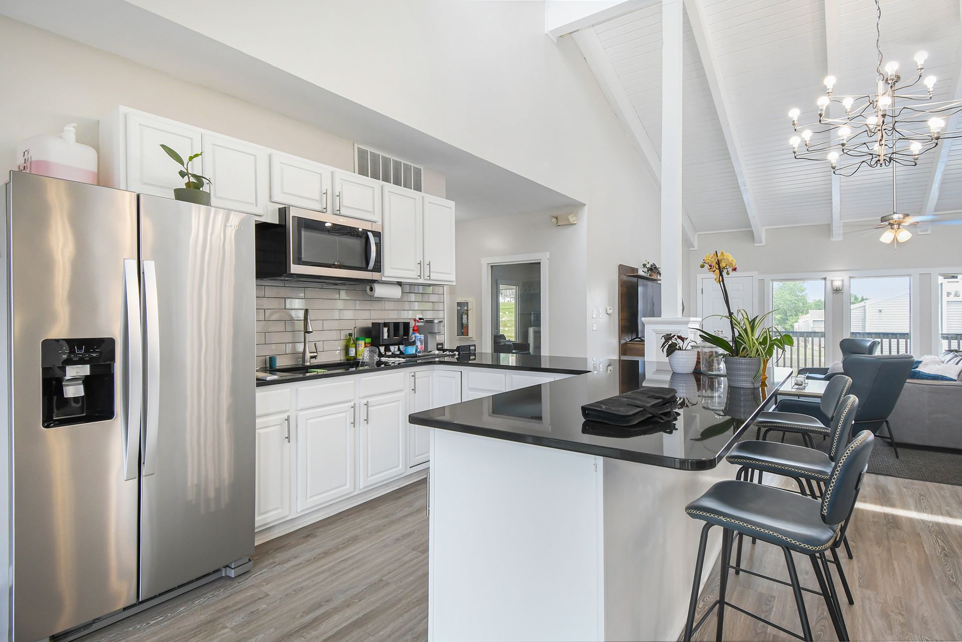 Bright kitchen with stainless steel appliances, white cabinets, and a black countertop island with stools.