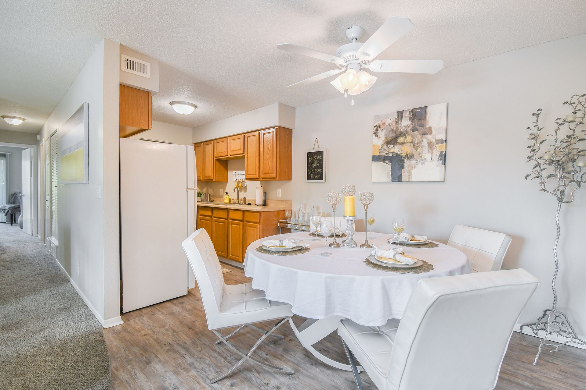 Dining area with round table set for a meal, white chairs, and kitchen in the background.