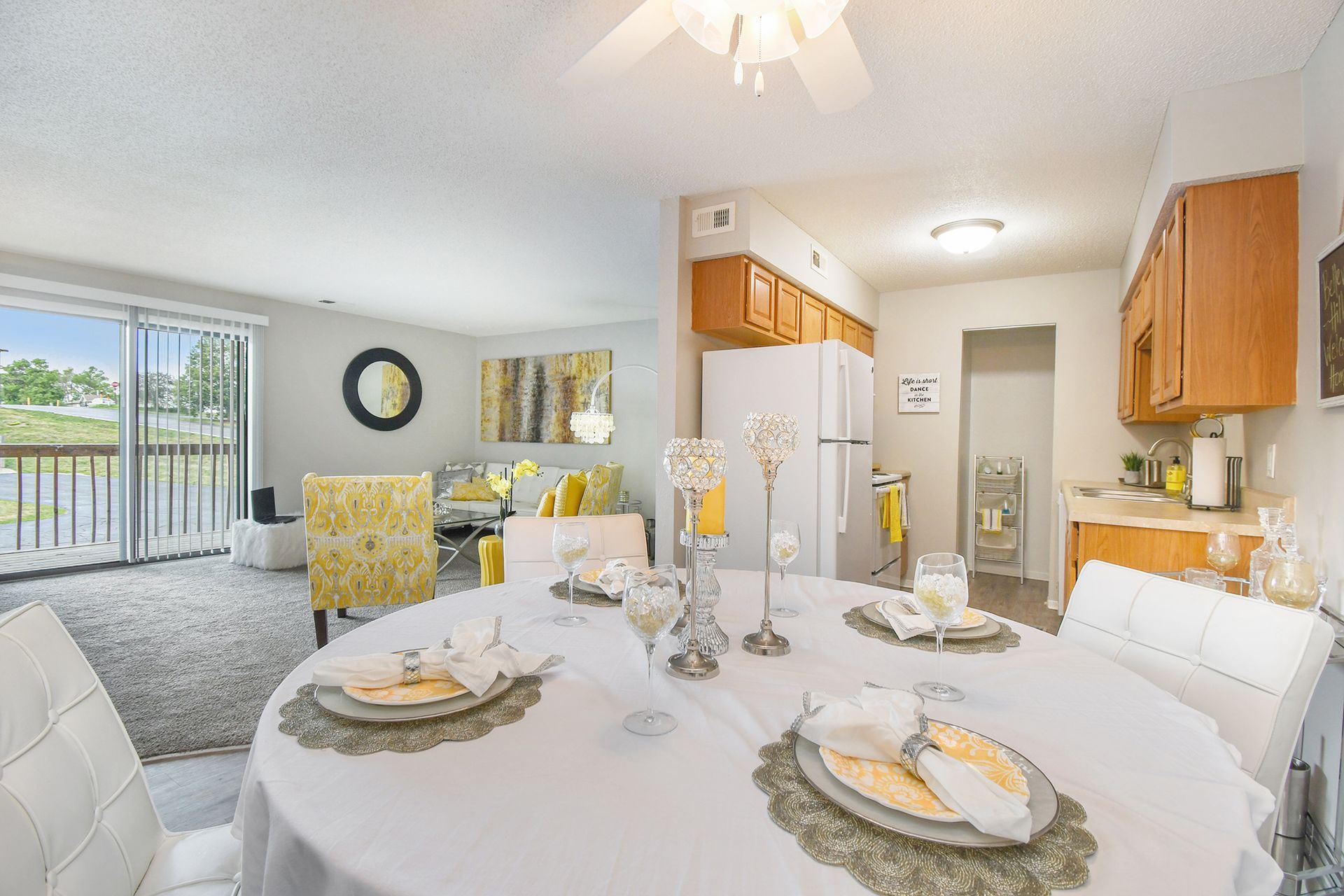 Dining area with round table set for a meal, opening to a living room with sliding doors and a view.