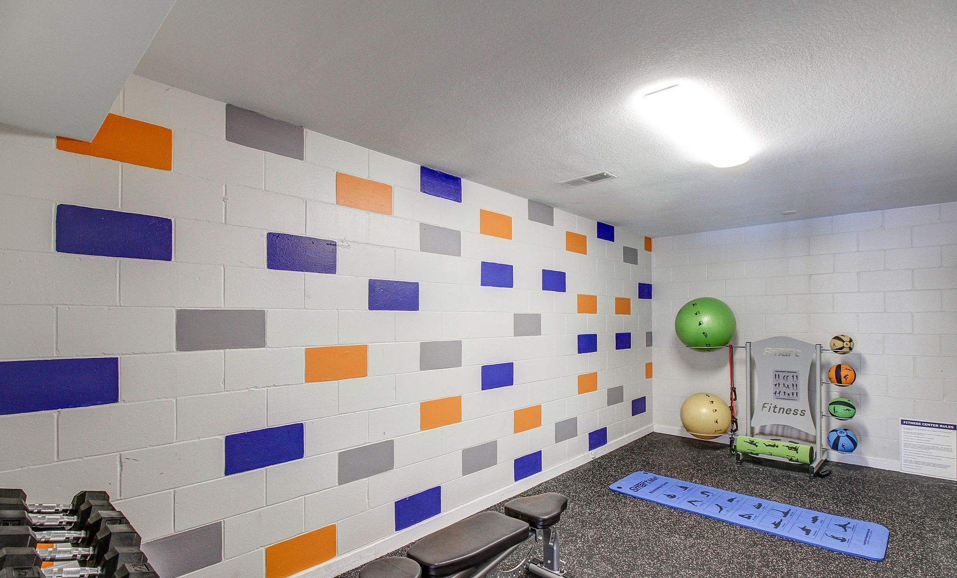 Gym with white block walls painted with orange, gray, and blue rectangles. Exercise equipment is present.