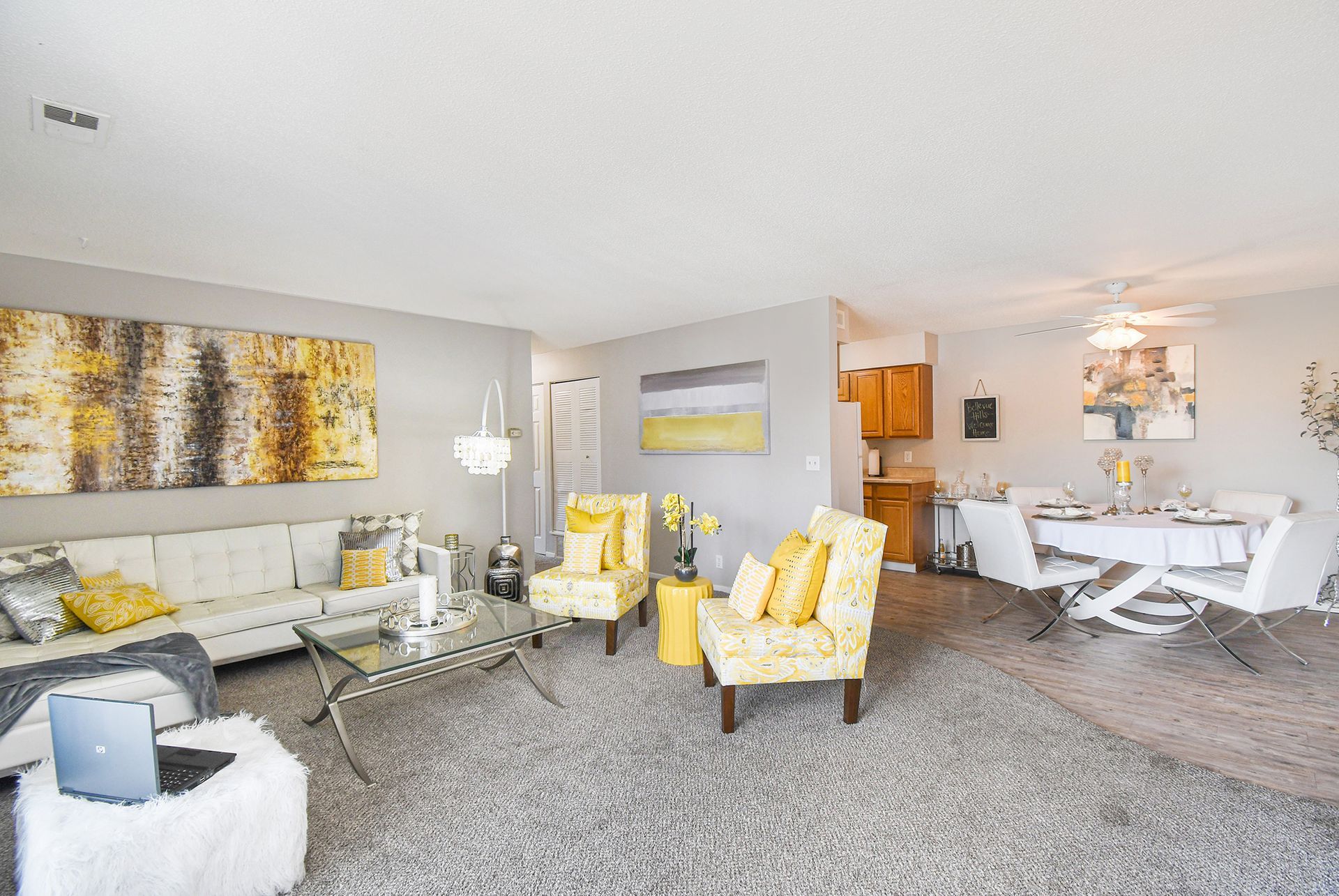 Living room with gray carpet, white couch, yellow accents, and a dining table.