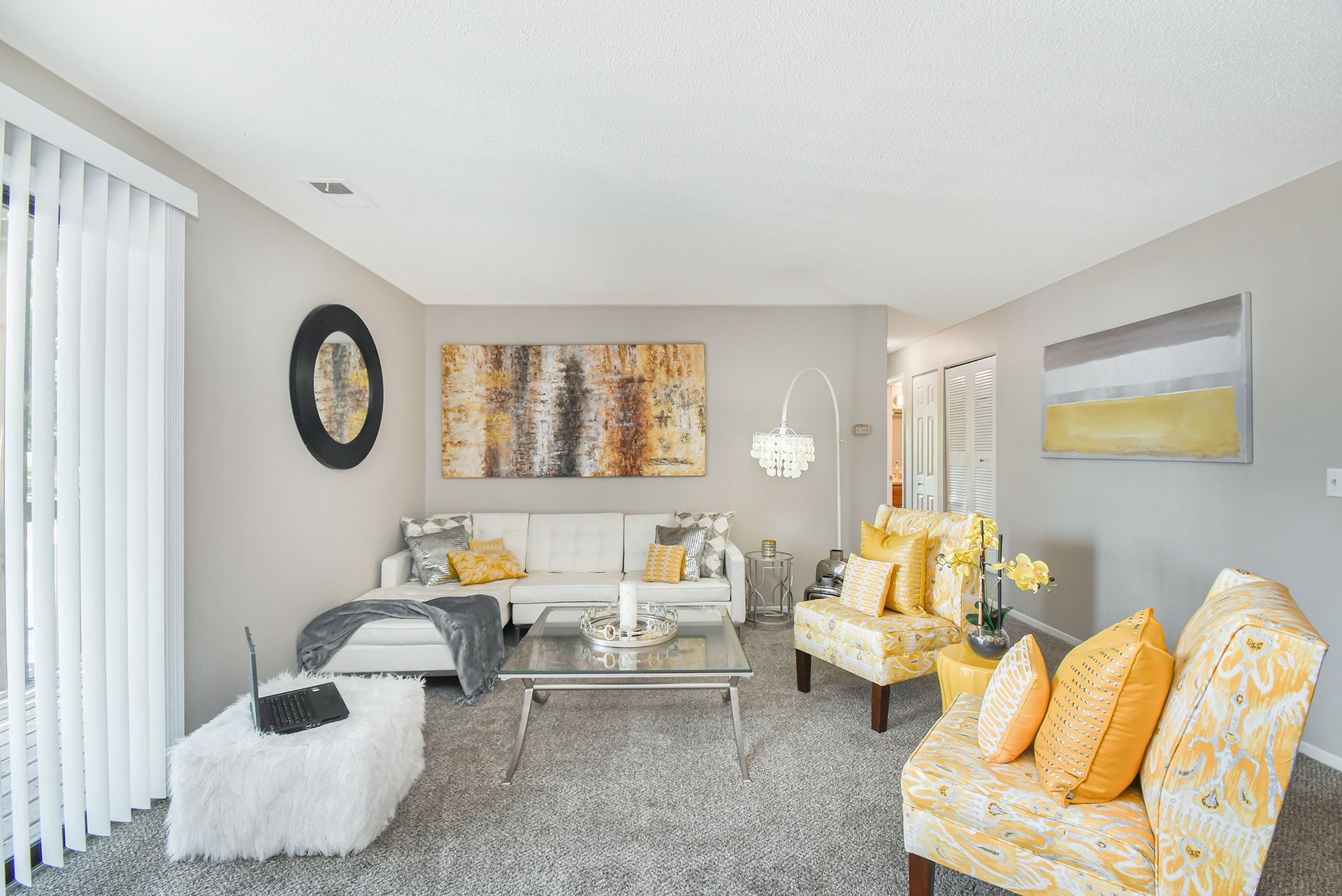 Living room with white sofa, yellow patterned chairs, grey carpet, and abstract art.