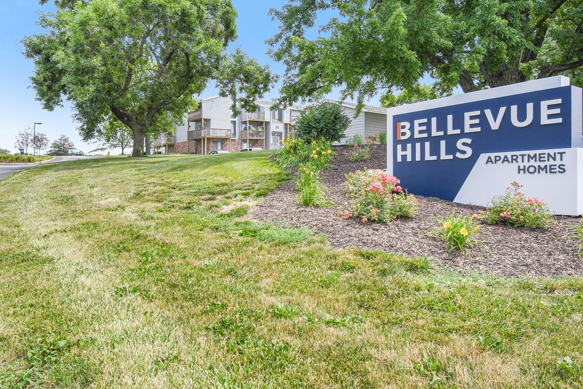 Sign for Bellevue Hills Apartment Homes on a grassy hill under a bright sky.