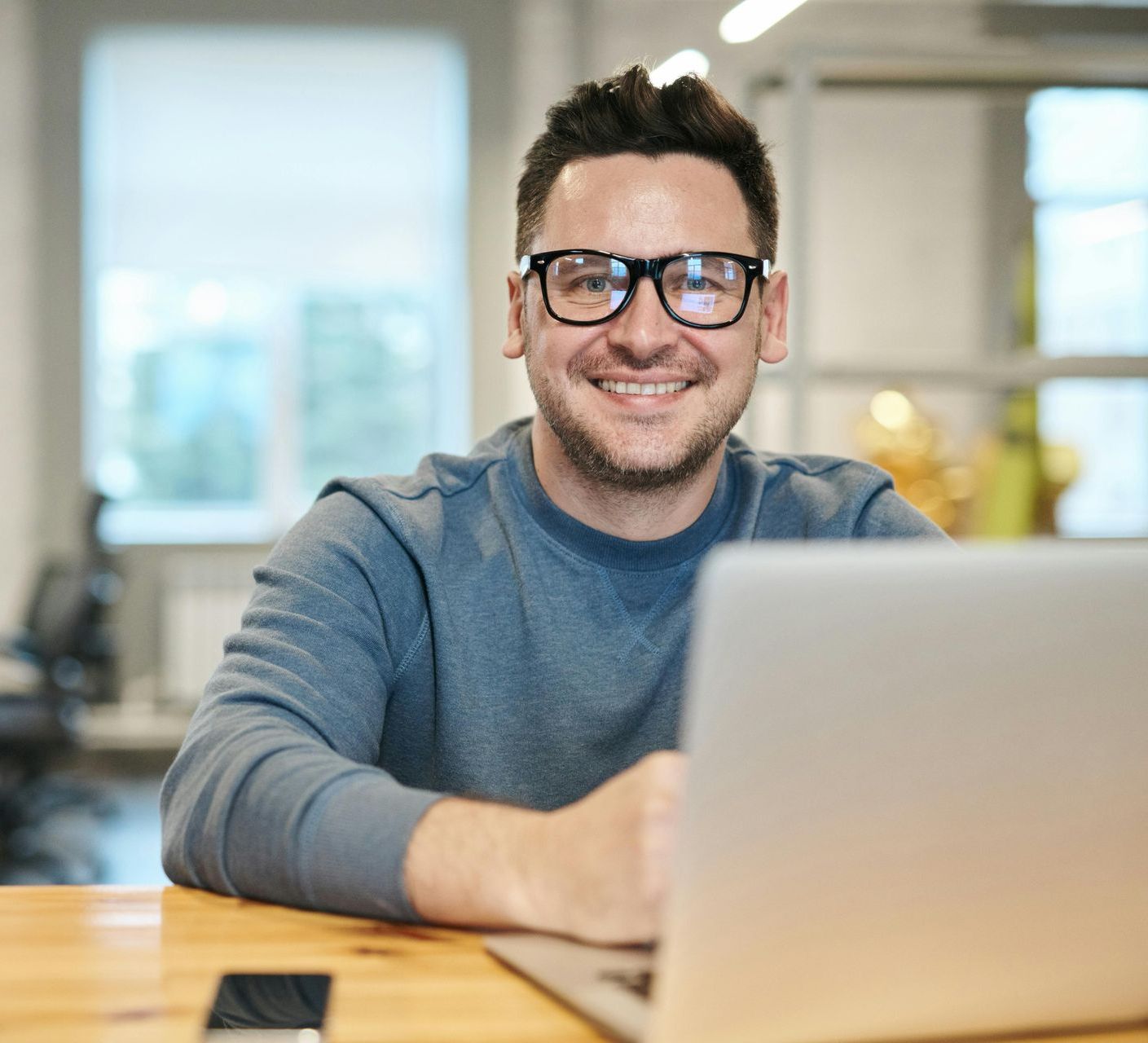 A man wearing glasses is sitting at a table using a laptop computer.