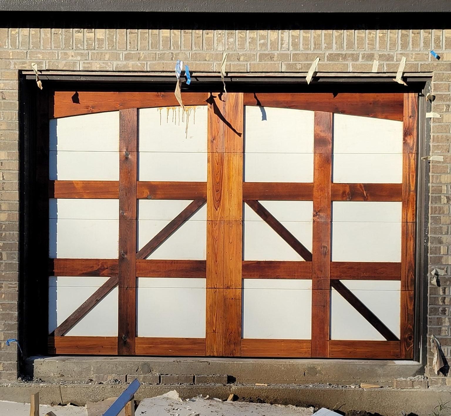 Wooden garage doors with white panels, installed in a brick frame, still under construction.