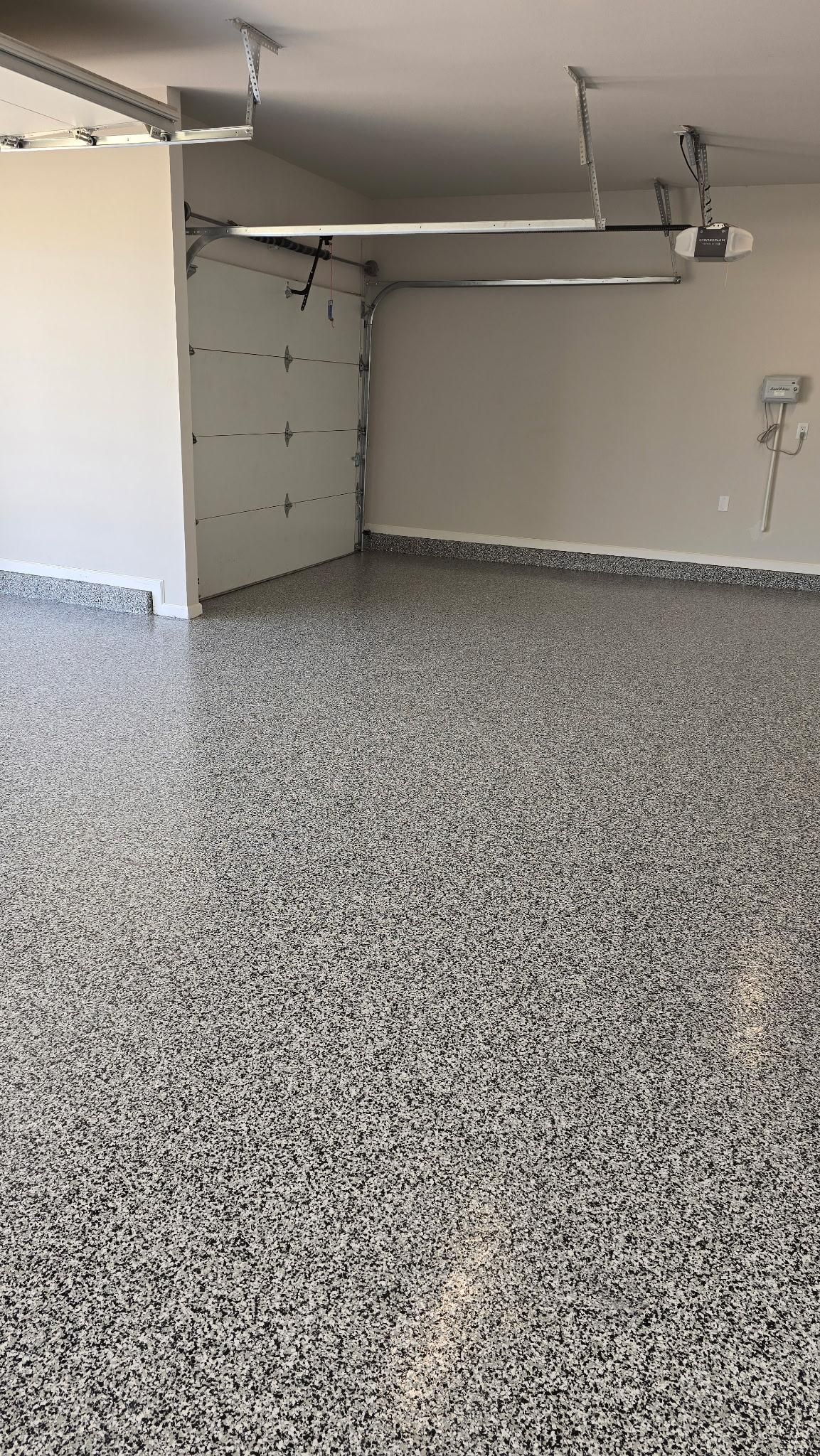 Empty garage with a speckled epoxy floor, white walls, and the garage door partially open.