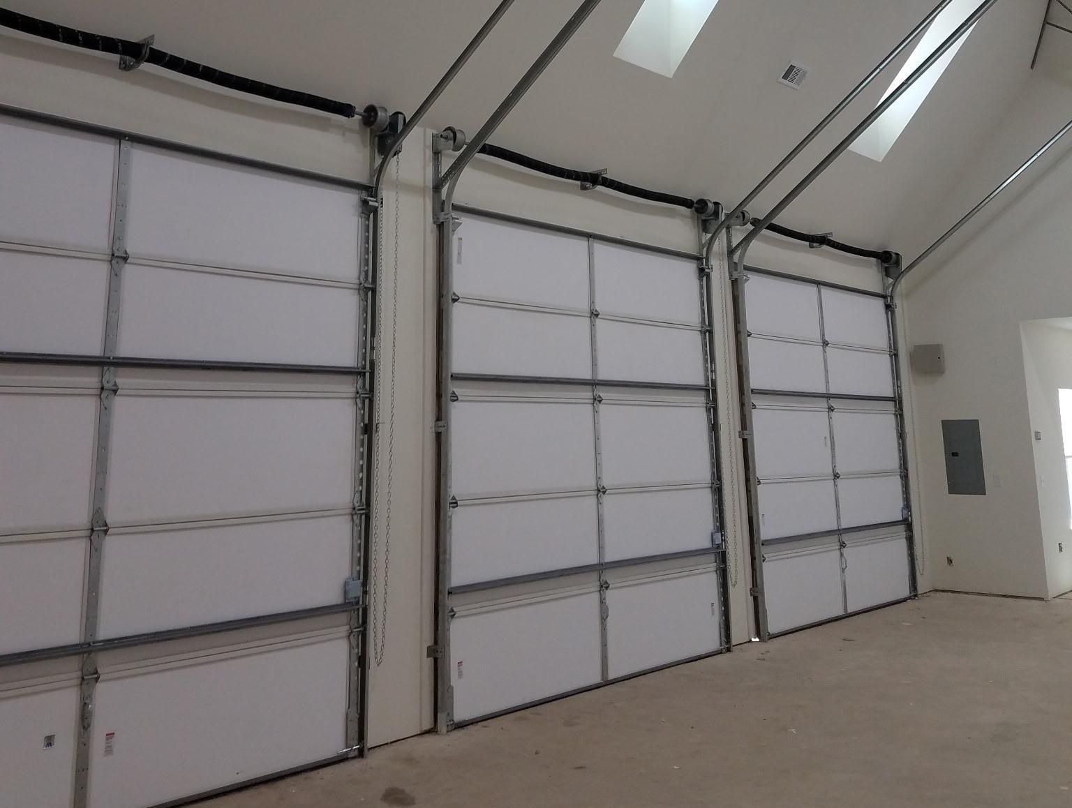 Three large white garage doors in a building with an angled ceiling. Each door has a silver frame and is closed.