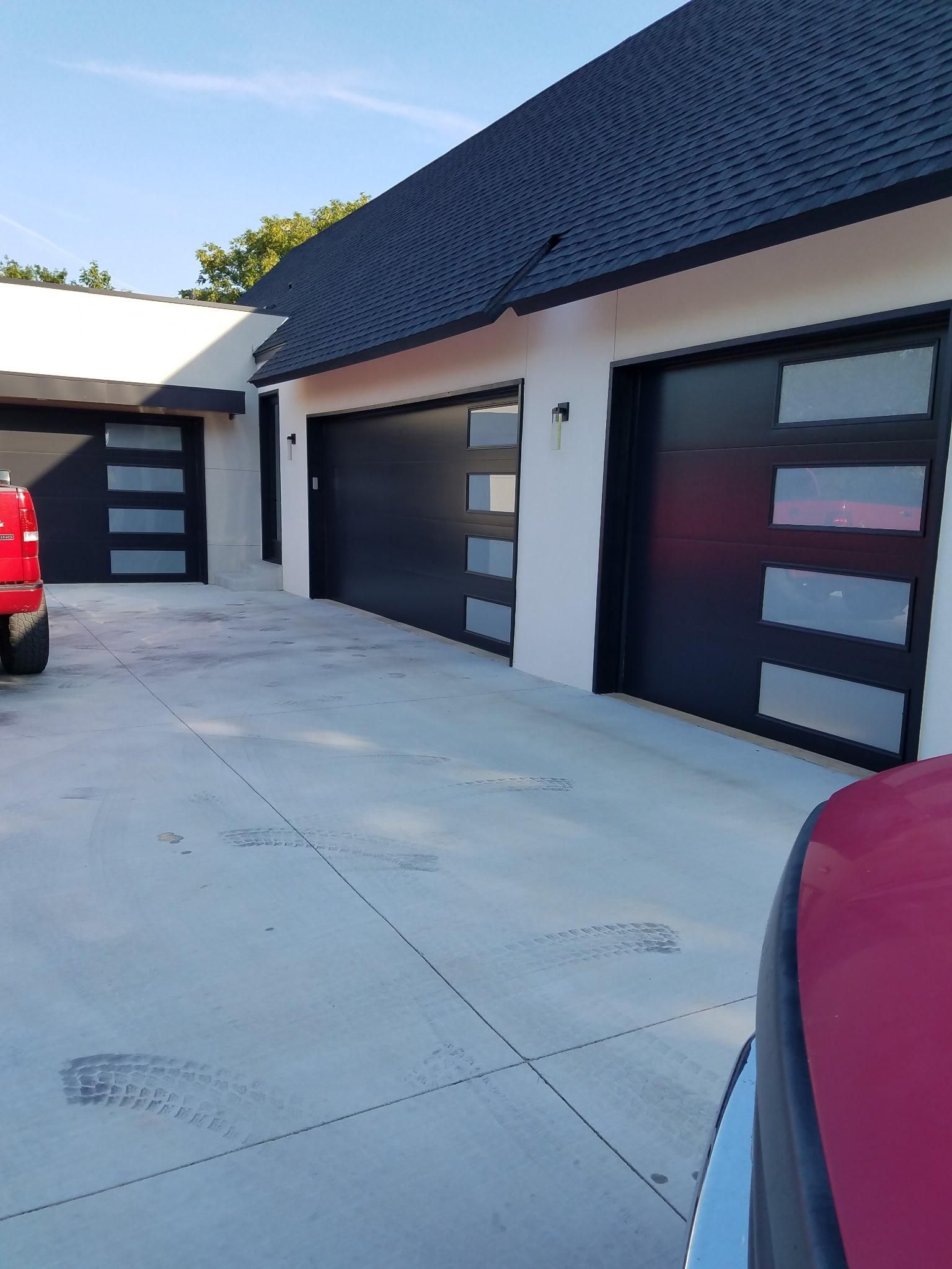 Three modern garage doors with frosted glass panels, black frames, on a white building.  Concrete driveway.