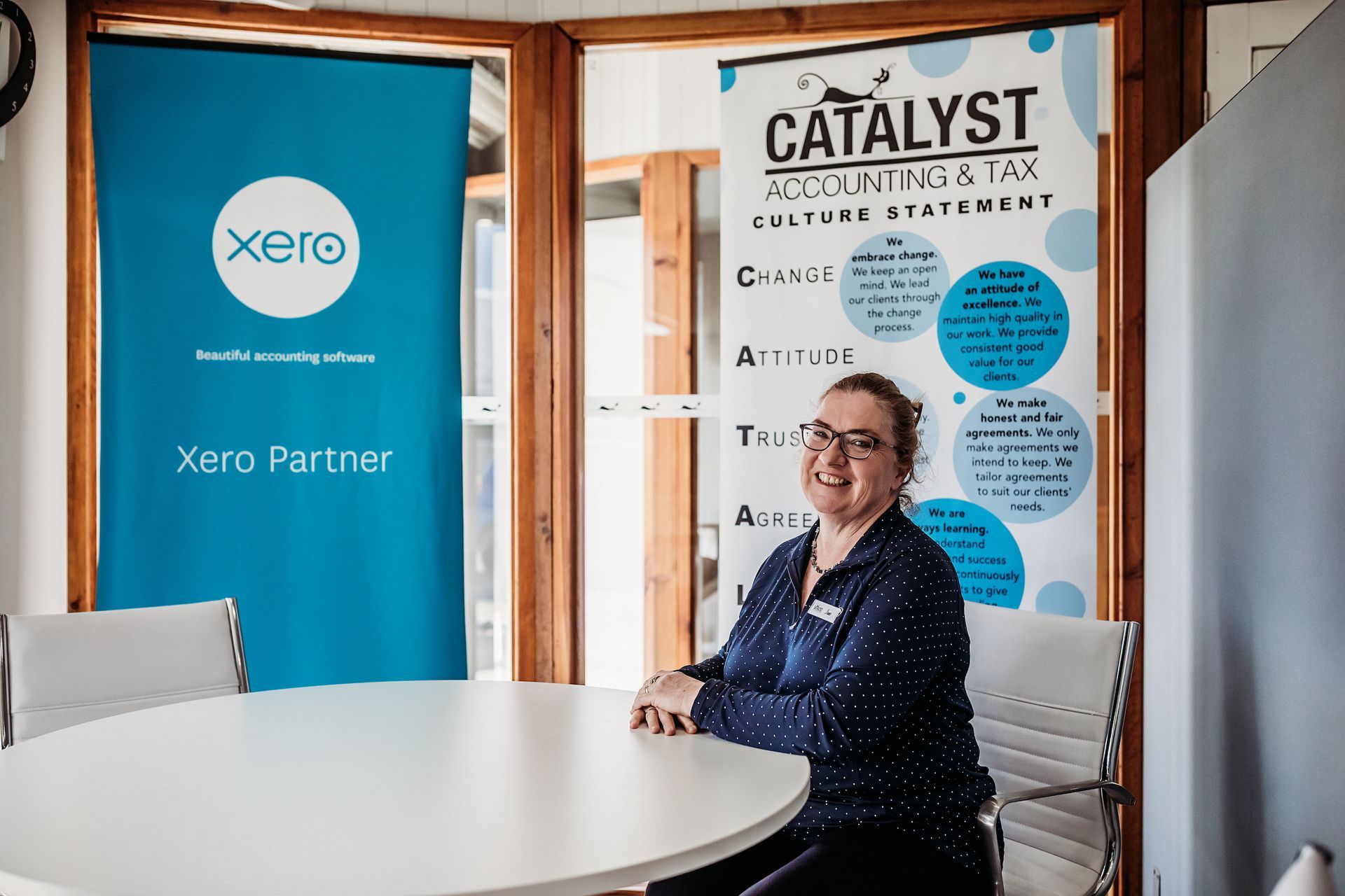 A Woman Is Sitting at A Table in Front of A Sign — Catalyst Accounting & Tax in Killarney, QLD