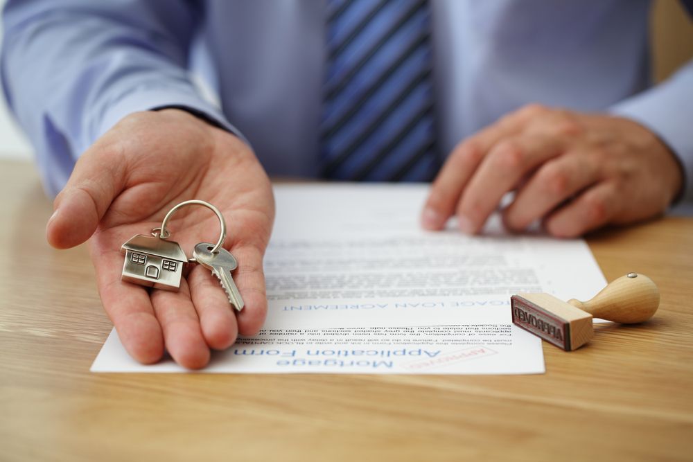 A Man is Holding a Pair of Keys in His Hand in Front of a Form — Chris Trevor & Associates in Gladstone Central, QLD