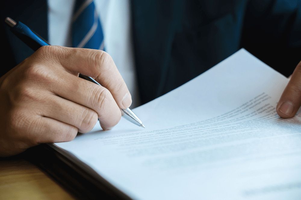 A Man in a Suit and Tie is Writing on a Piece of Paper With a Pen — Chris Trevor & Associates in Gladstone Central, QLD