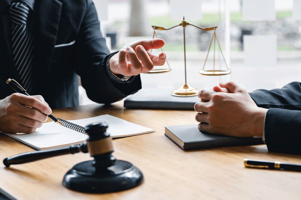 Two Men Are Sitting at a Table With a Gavel and Scales of Justice — Chris Trevor & Associates in Moranbah, QLD