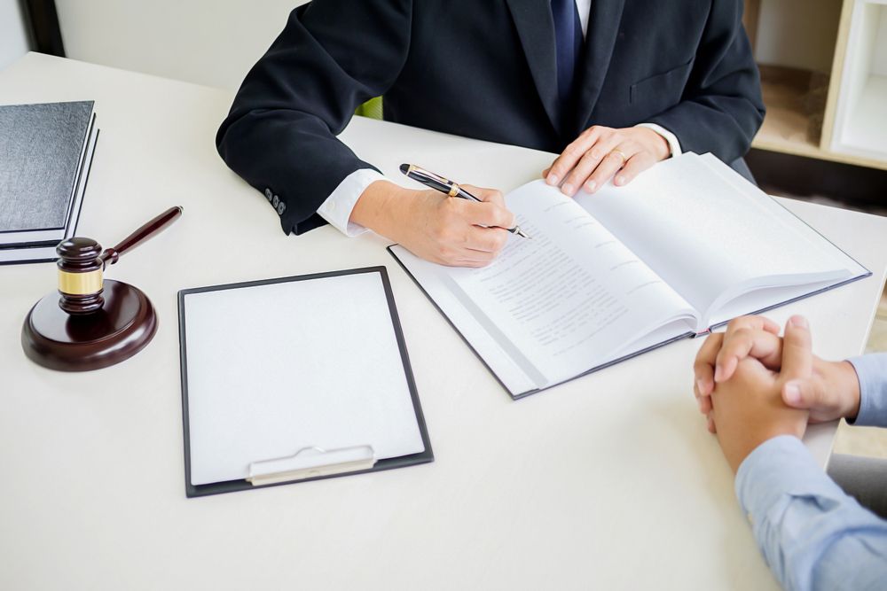 A Lawyer is Sitting at a Table With a Client and Signing a Document — Chris Trevor & Associates in Emerald, QLD