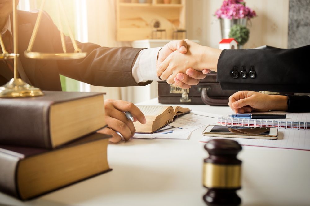 A Lawyer is Shaking Hands With a Client While Sitting at a Desk — Chris Trevor & Associates in Rockhampton, QLD