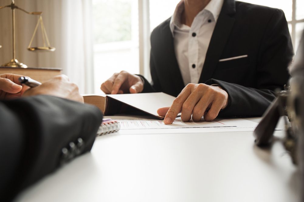 A Man in a Suit is Sitting at a Table Looking at a Piece of Paper — Chris Trevor & Associates in Gladstone Central, QLD