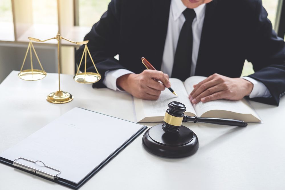 A Man in a Suit and Tie is Sitting at a Table With a Book and a Gavel — Chris Trevor & Associates in Rockhampton, QLD